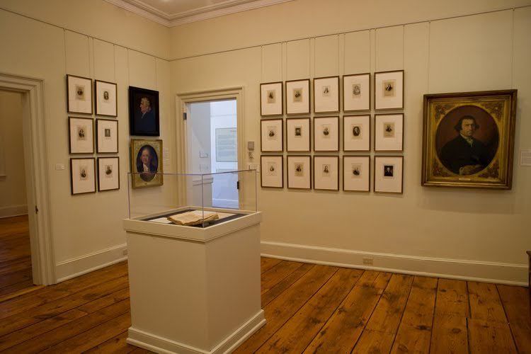 Art gallery with portraits on the walls, wooden floor, and a display case in the center.