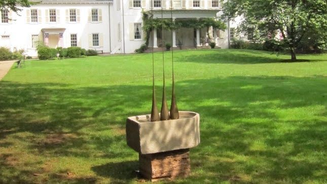 A white building with a grassy lawn, featuring a concrete sculpture with tall, thin stalks.