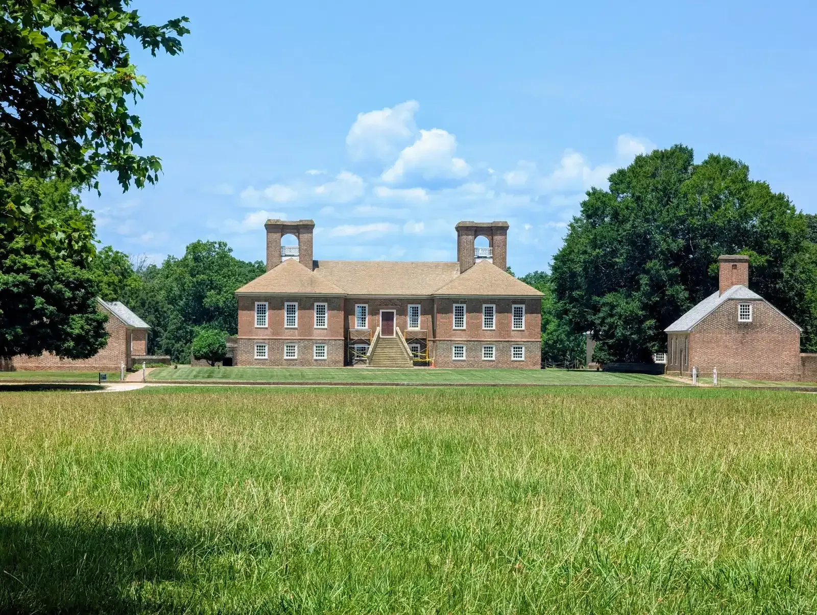 A historic brick plantation house with two prominent chimneys, surrounded by green fields and trees under a blue sky.