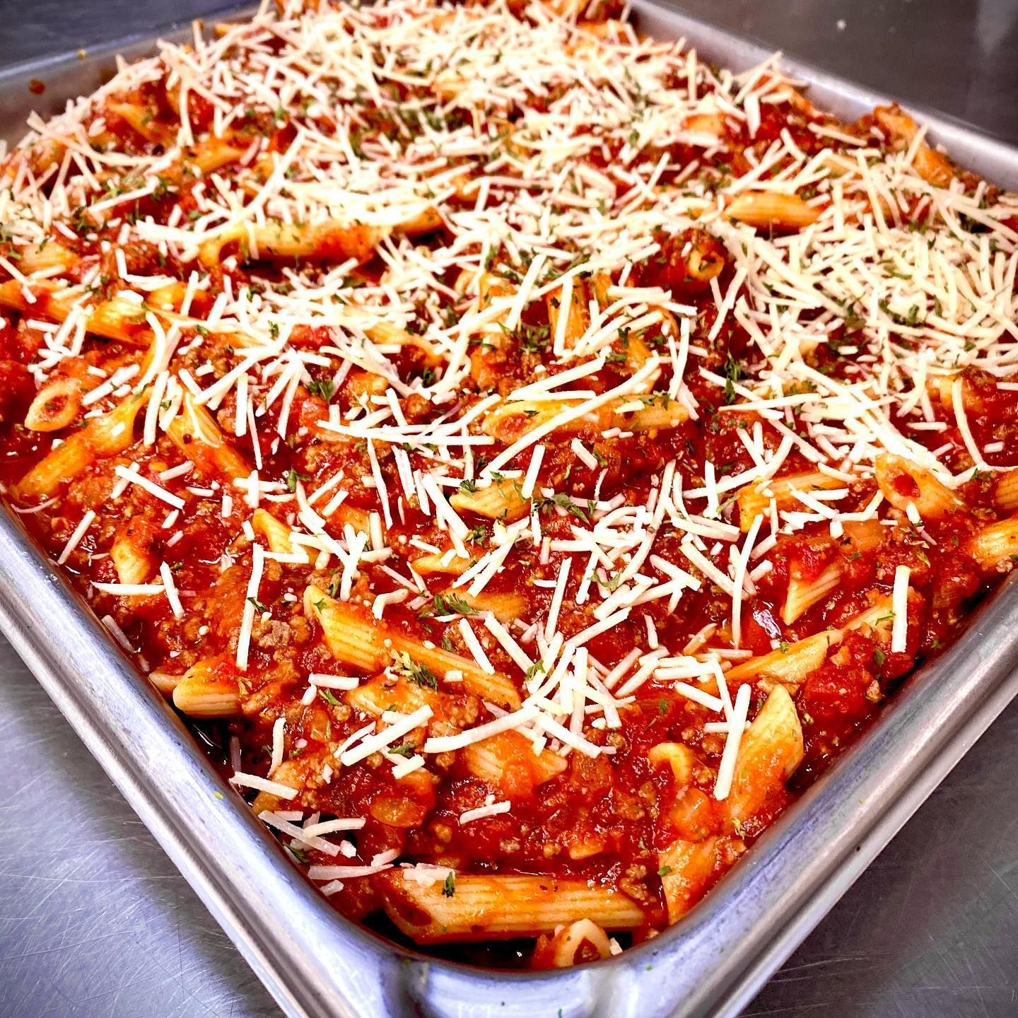 Pasta bake in a metal pan, topped with shredded cheese.