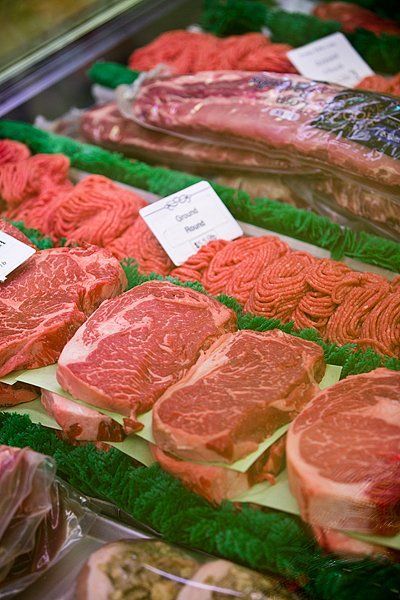 Display case filled with various cuts of raw red meat, including steaks and ground beef.