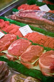 Display case filled with various cuts of raw red meat, including steaks and ground beef.