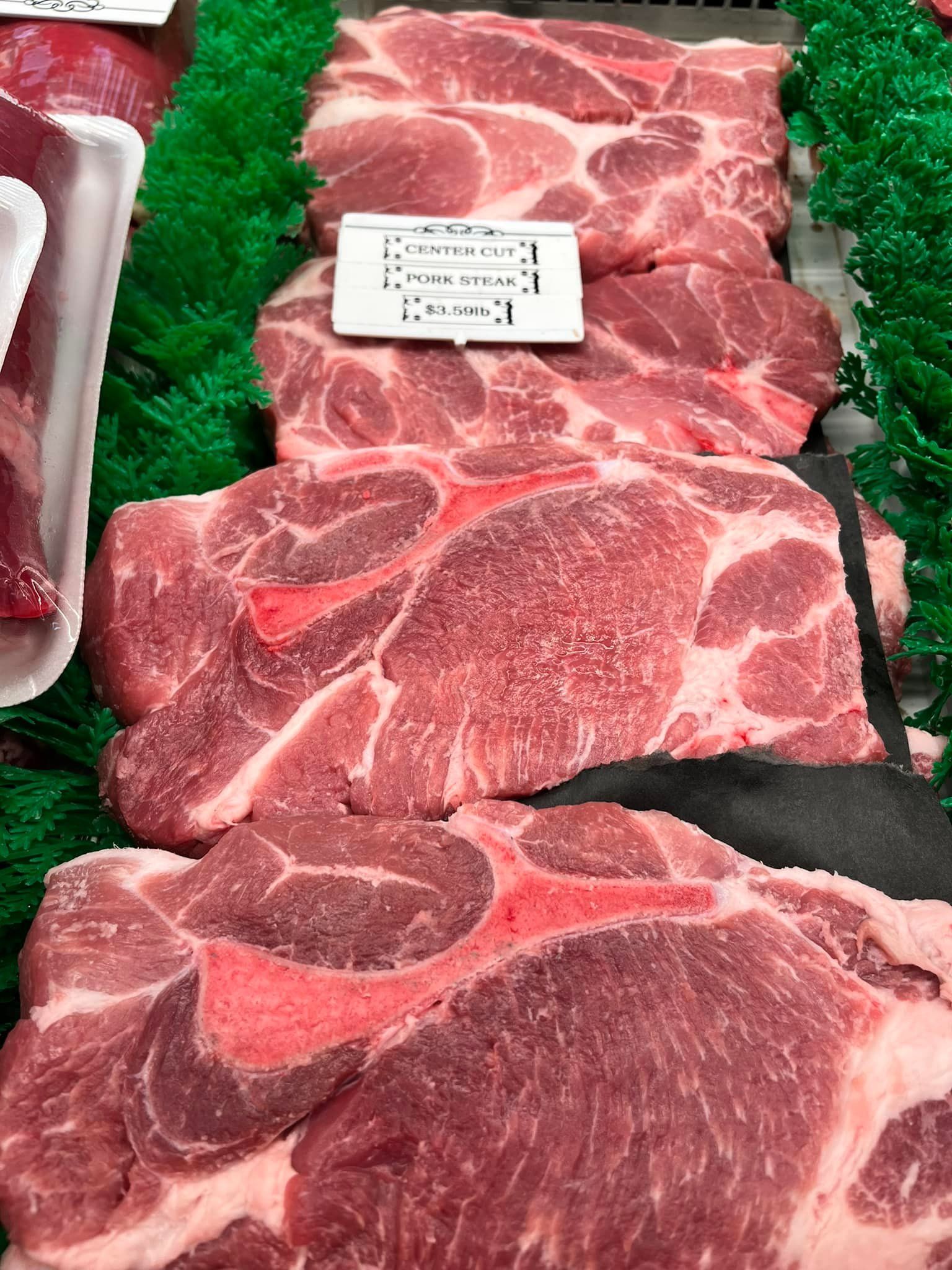 Pork shoulder steaks displayed in a refrigerated case. Red meat with marbling and bone visible.