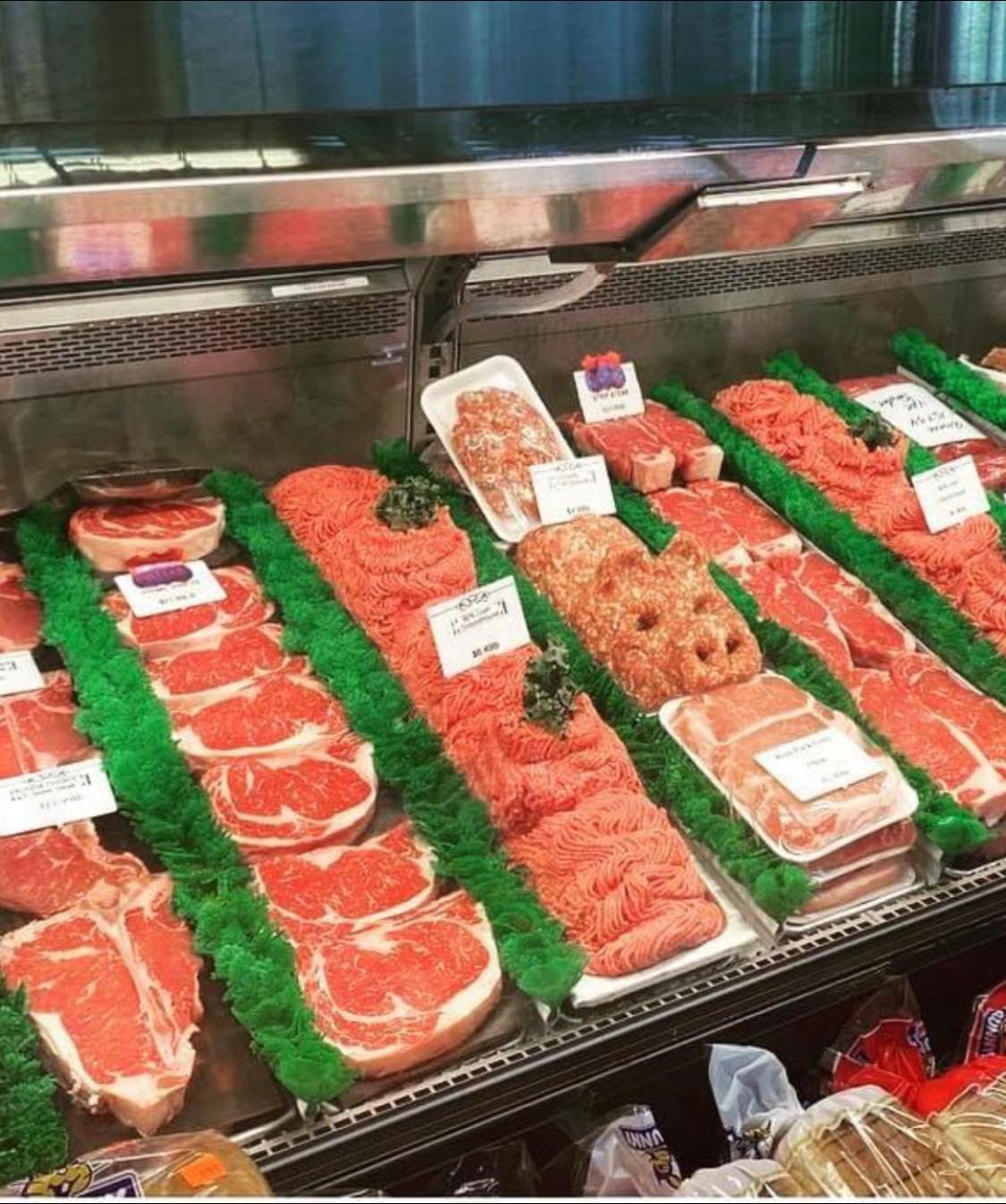 Meat display in a refrigerated case. Various cuts of red meat, in white trays, on green plastic, in a grocery store.
