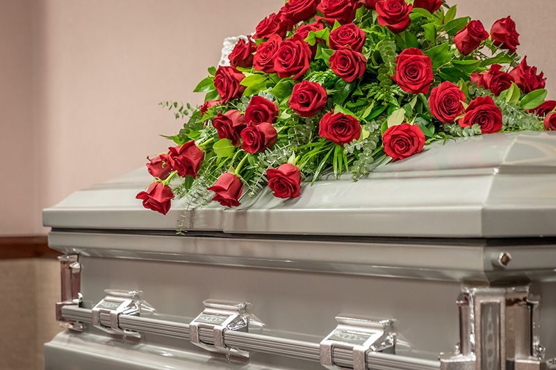 Silver casket topped with red roses at a funeral setting