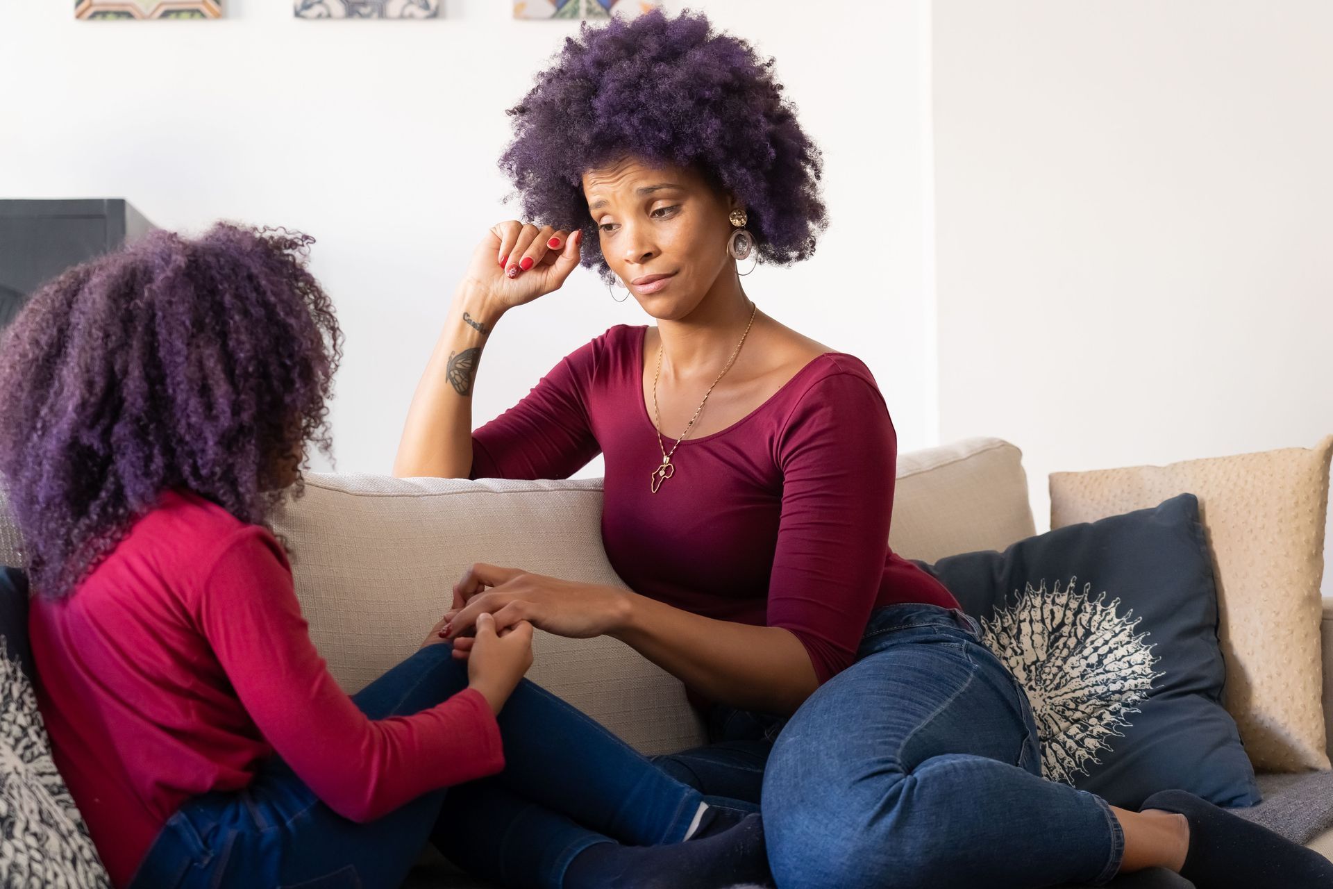 Two people sitting on a white couch, talking quietly in a bright living room