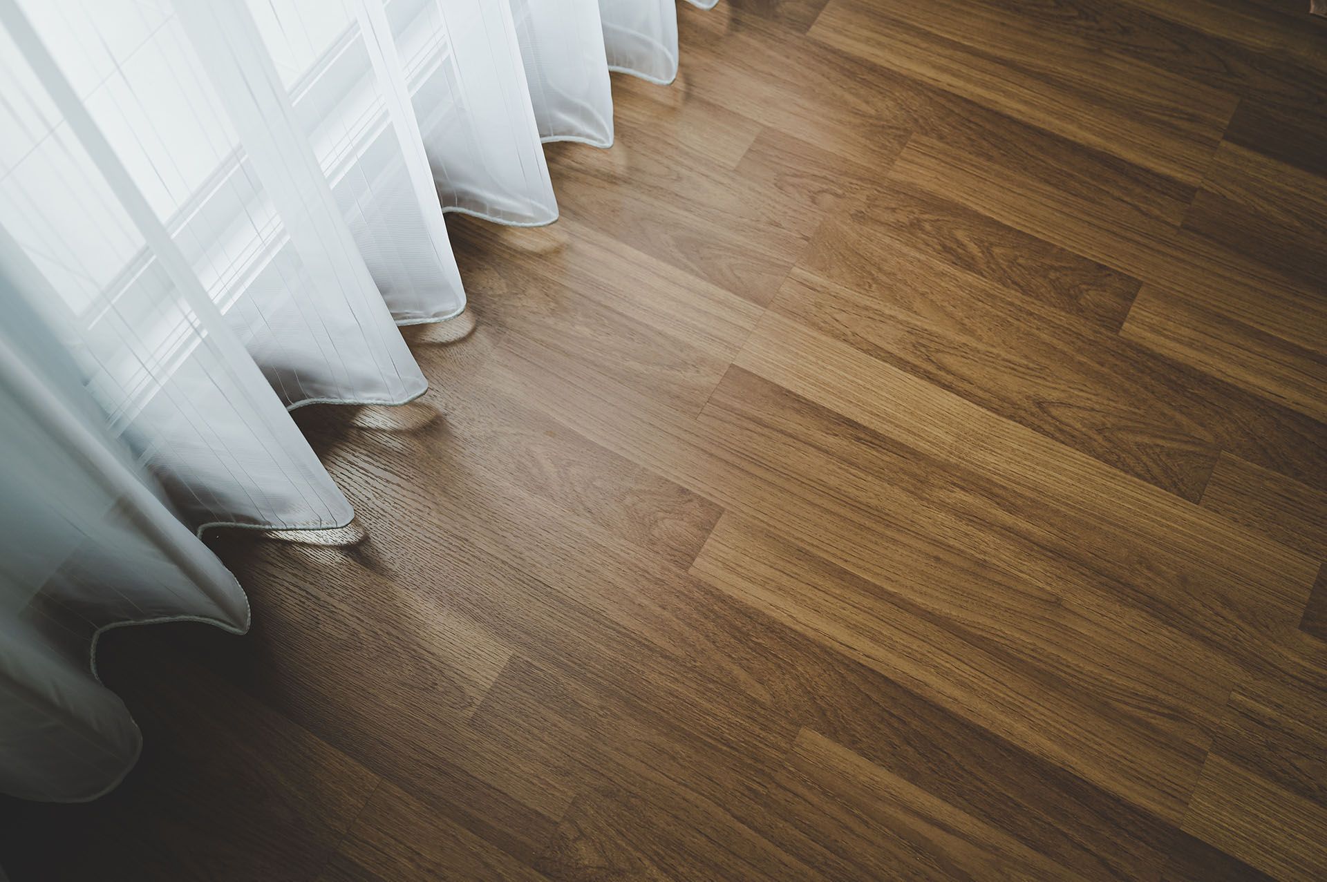 White sheer curtains beside a sunlit wooden floor with light patterns from the window