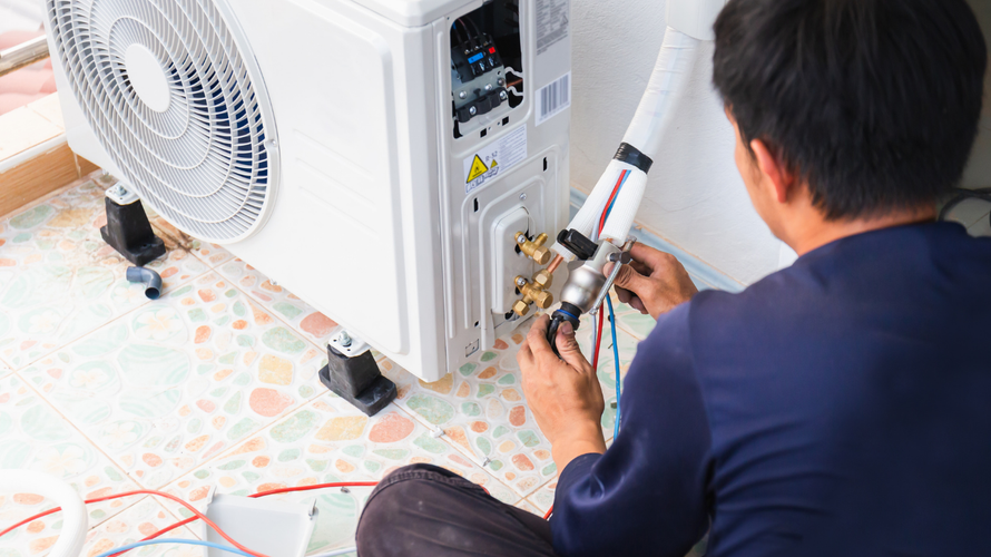 Technician repairing an outdoor air conditioner unit with tools on a tiled floor.