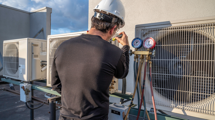 Technician inspecting HVAC units with gauges on a rooftop under a blue sky