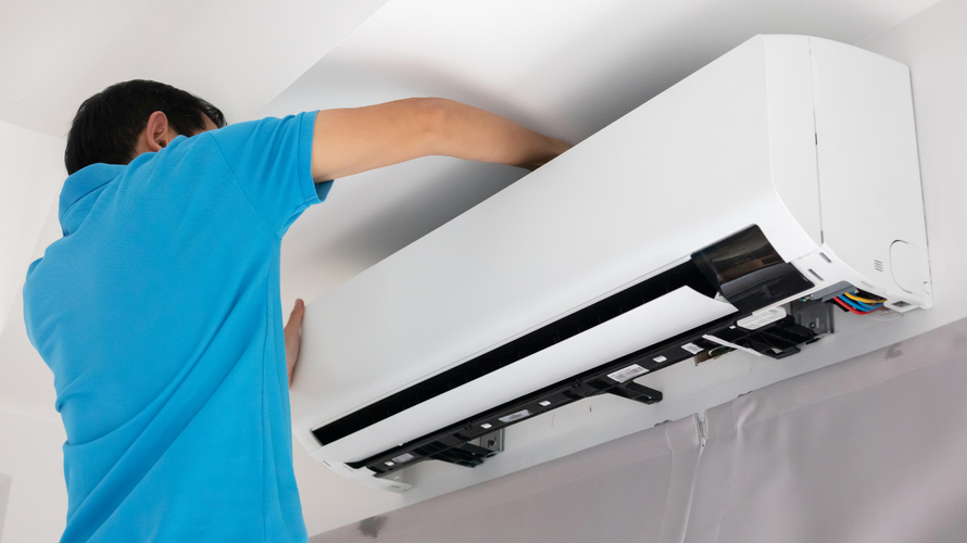 Technician in blue shirt installing a wall-mounted air conditioner indoors