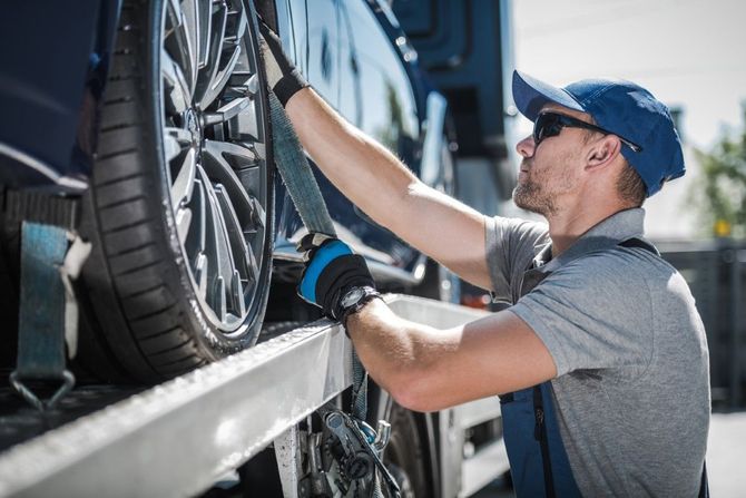 Man in a blue cap tightening a car wheel on a truck transport trailer