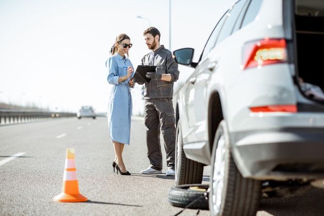 Driver and officer talking beside a silver SUV on a roadside, with an orange traffic cone nearby.
