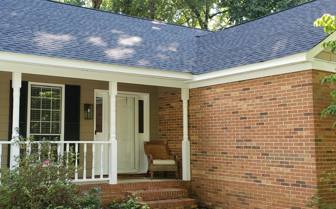 Brick house with porch, white trim, dark roof, and steps leading to the front door.