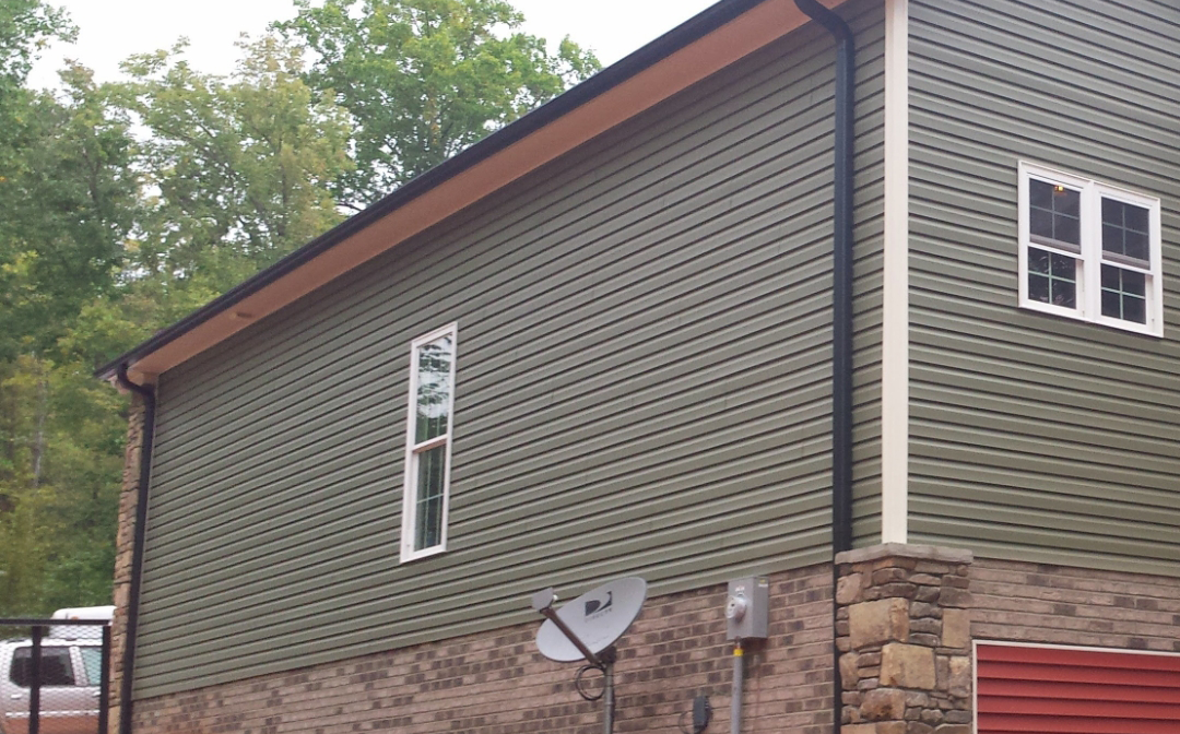 Green siding on a two-story house with a stone foundation, white-framed windows, and a satellite dish.