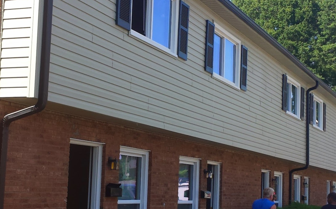 Two-story brick and beige siding apartment building with open windows and black shutters.