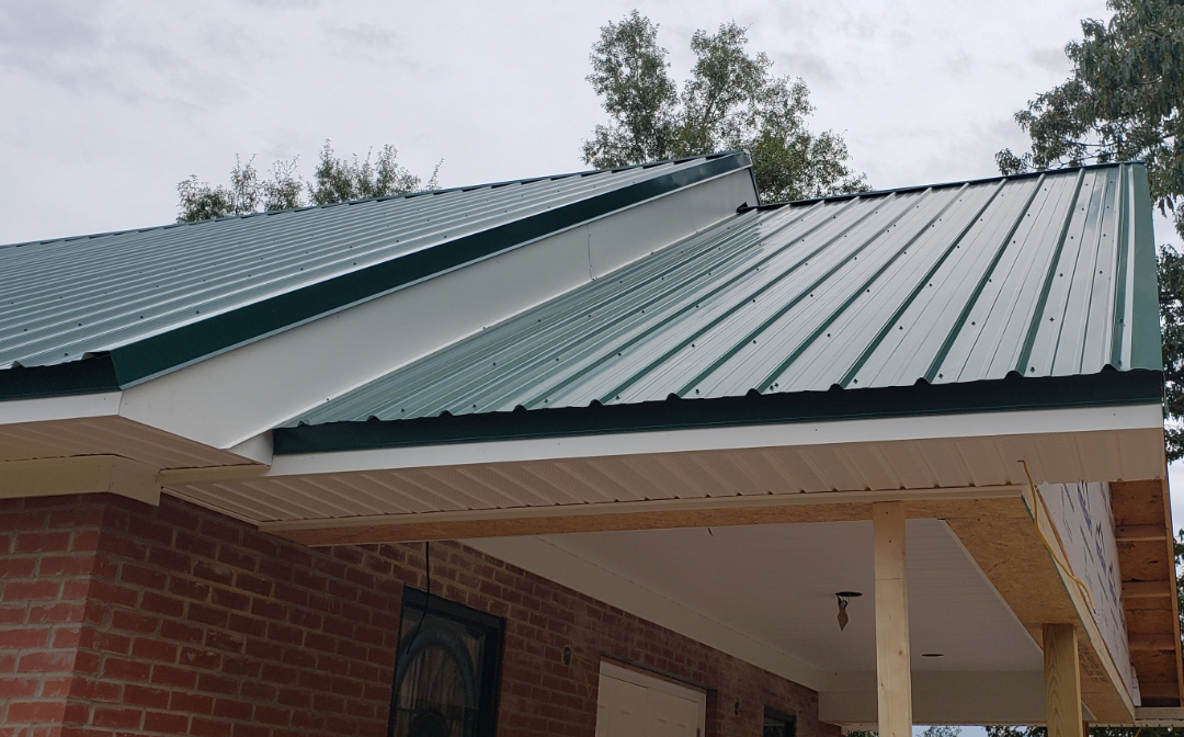 Green metal roof on a brick building with white trim and a porch under a cloudy sky.