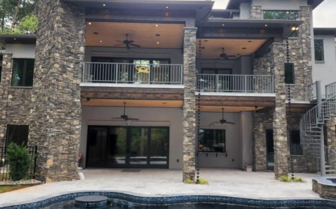 Back of a multi-story modern house with stone pillars, a pool, and a spiral staircase.