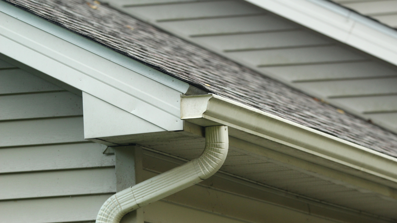 White gutters and downspout on a house with gray siding and roof.