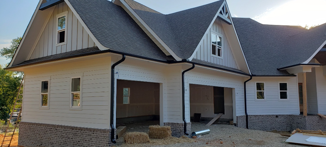 A house with a light-colored exterior, dark roof, and garage under construction.