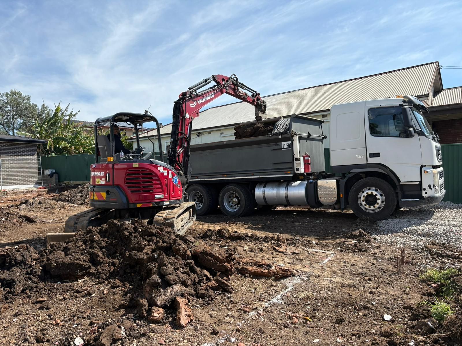 Red excavator loading dirt into a dump truck on a construction site. Blue sky.
