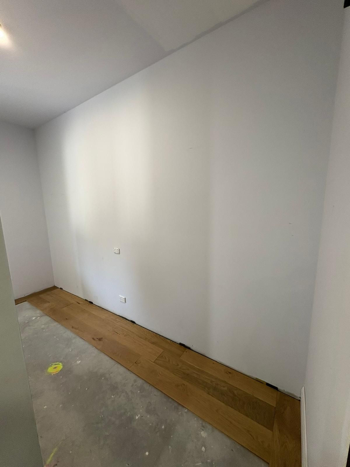 Empty room with a white wall and wood flooring. Concrete floor visible.