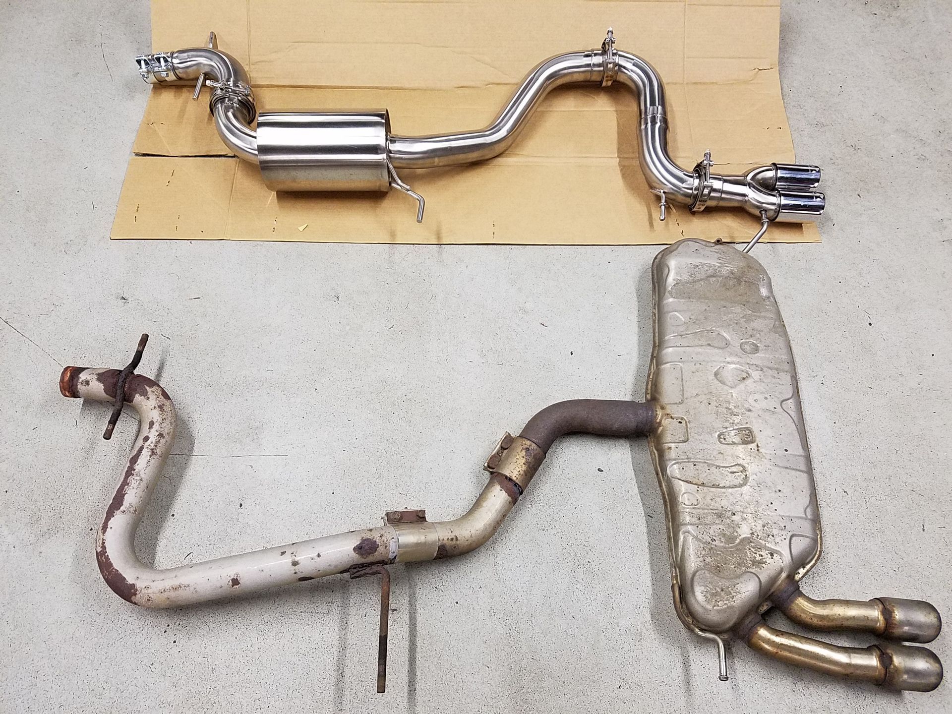 Two car exhaust systems; new shiny metal one above, old rusty one below. | Autobahn Performance Inc