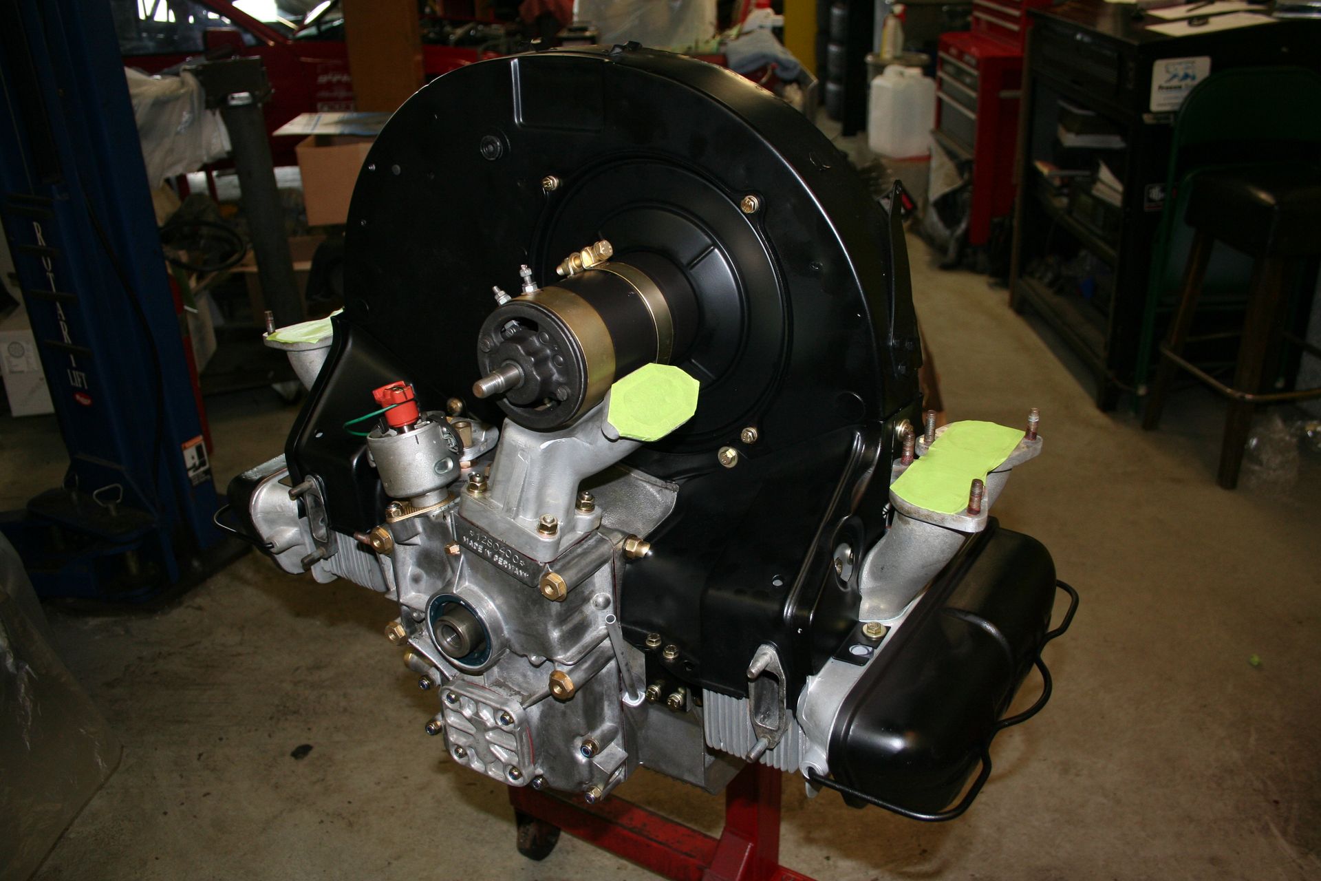 Black and silver Volkswagen engine on a stand, with air-cooled cylinders, various attached components, and black shroud. | Autobahn Performance Inc