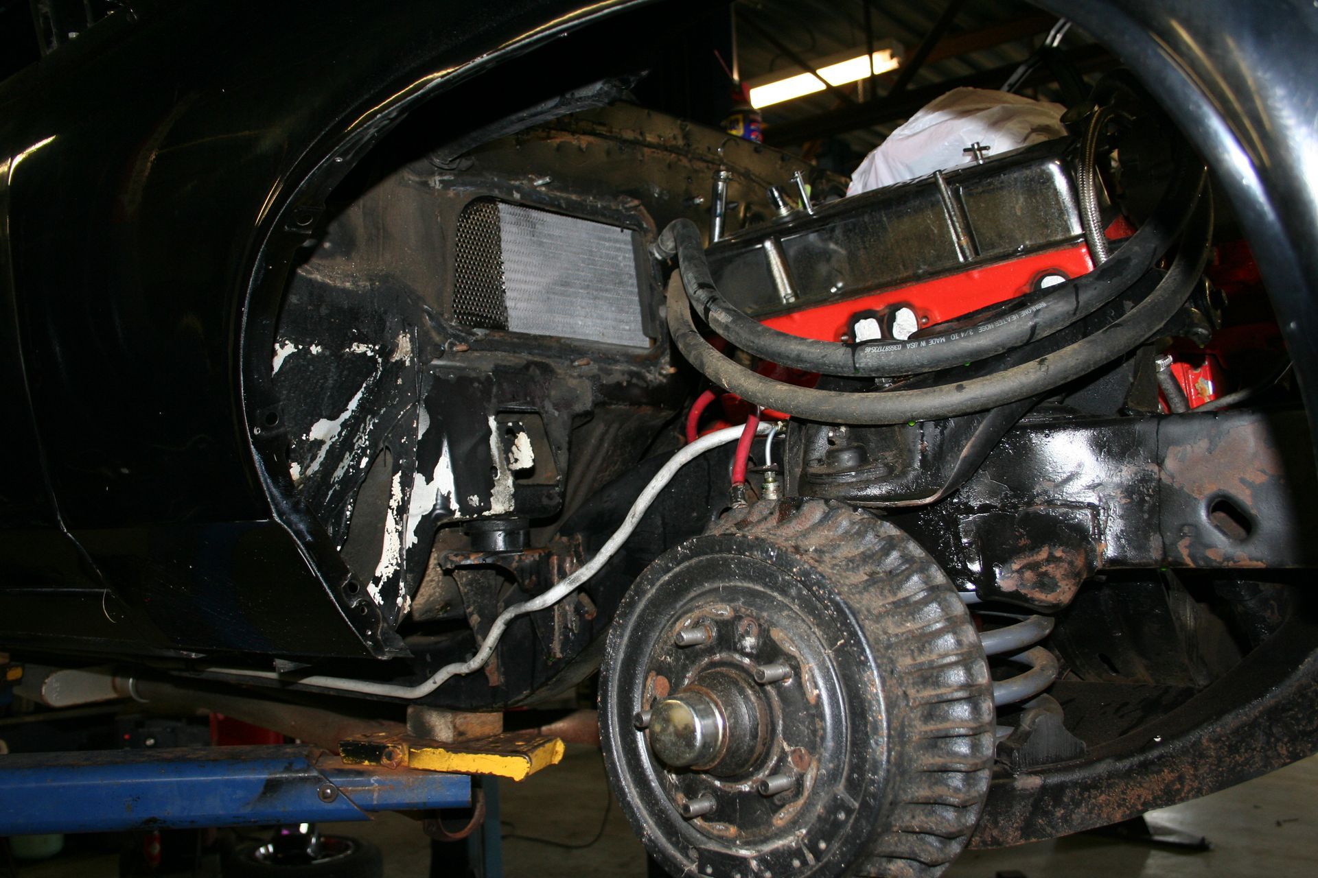 Black car's wheel well open, exposing engine and suspension. Technician working on car, indoors. | Autobahn Performance Inc
