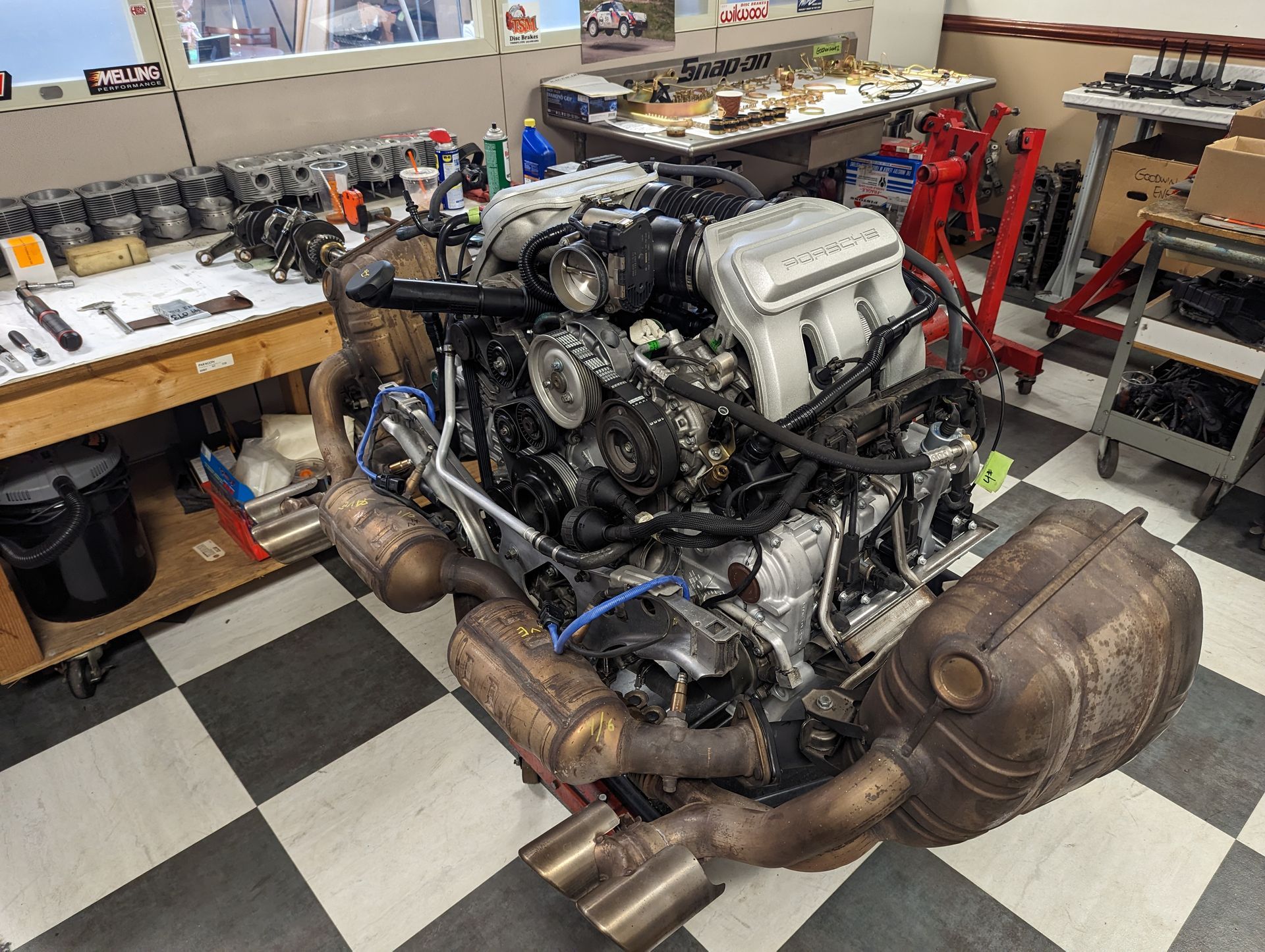 Engine, exhaust system, and components on a shop floor. Gray and silver parts, black checkerboard floor. | Autobahn Performance Inc