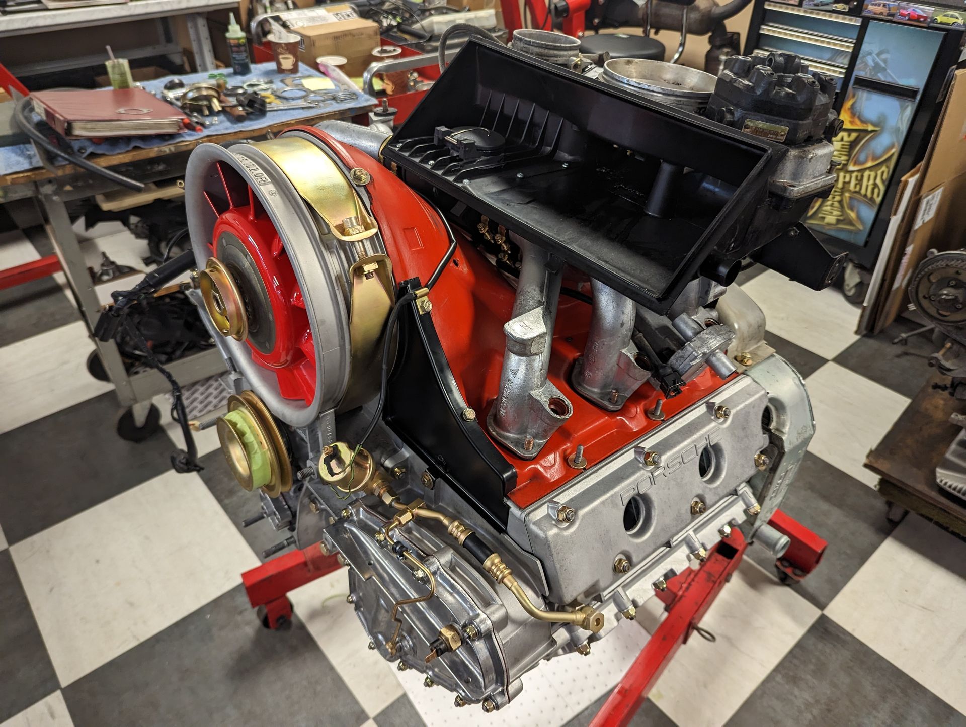 Porsche engine on a red stand, partially assembled. Red, silver, and gold components. | Autobahn Performance