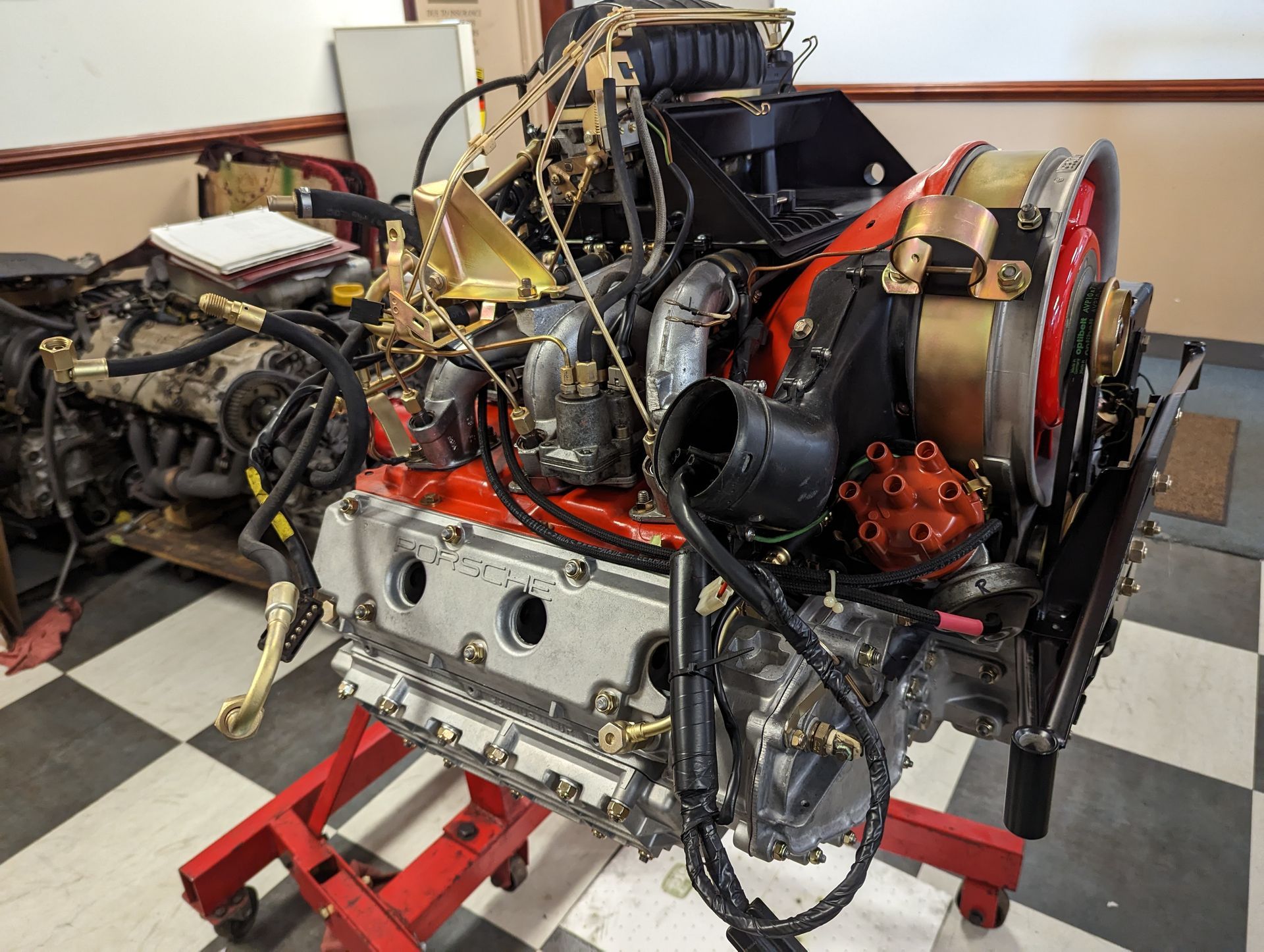 Porsche engine, red and silver, on a red stand, with black components and gold accents, in a workshop. | Autobahn Performance
