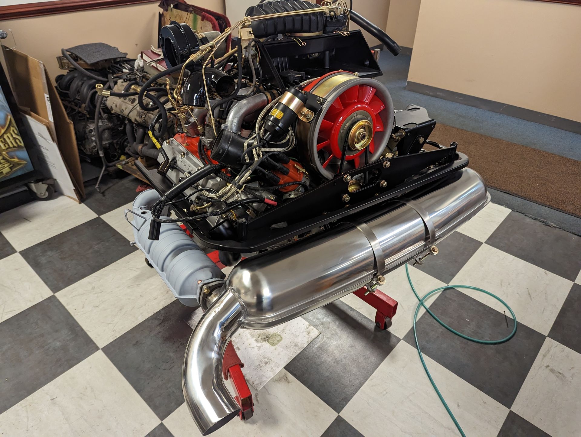 Porsche car engine with red fan, chrome exhaust, and wiring on a checkered floor. | Autobahn Performance