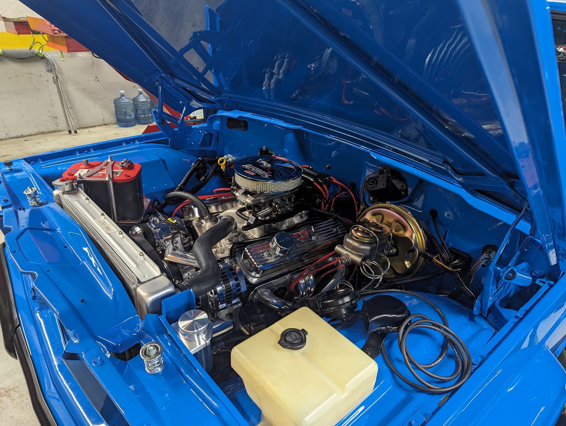 Blue car engine bay with black engine, chrome details, and white coolant tank. | Autobahn Performance Inc