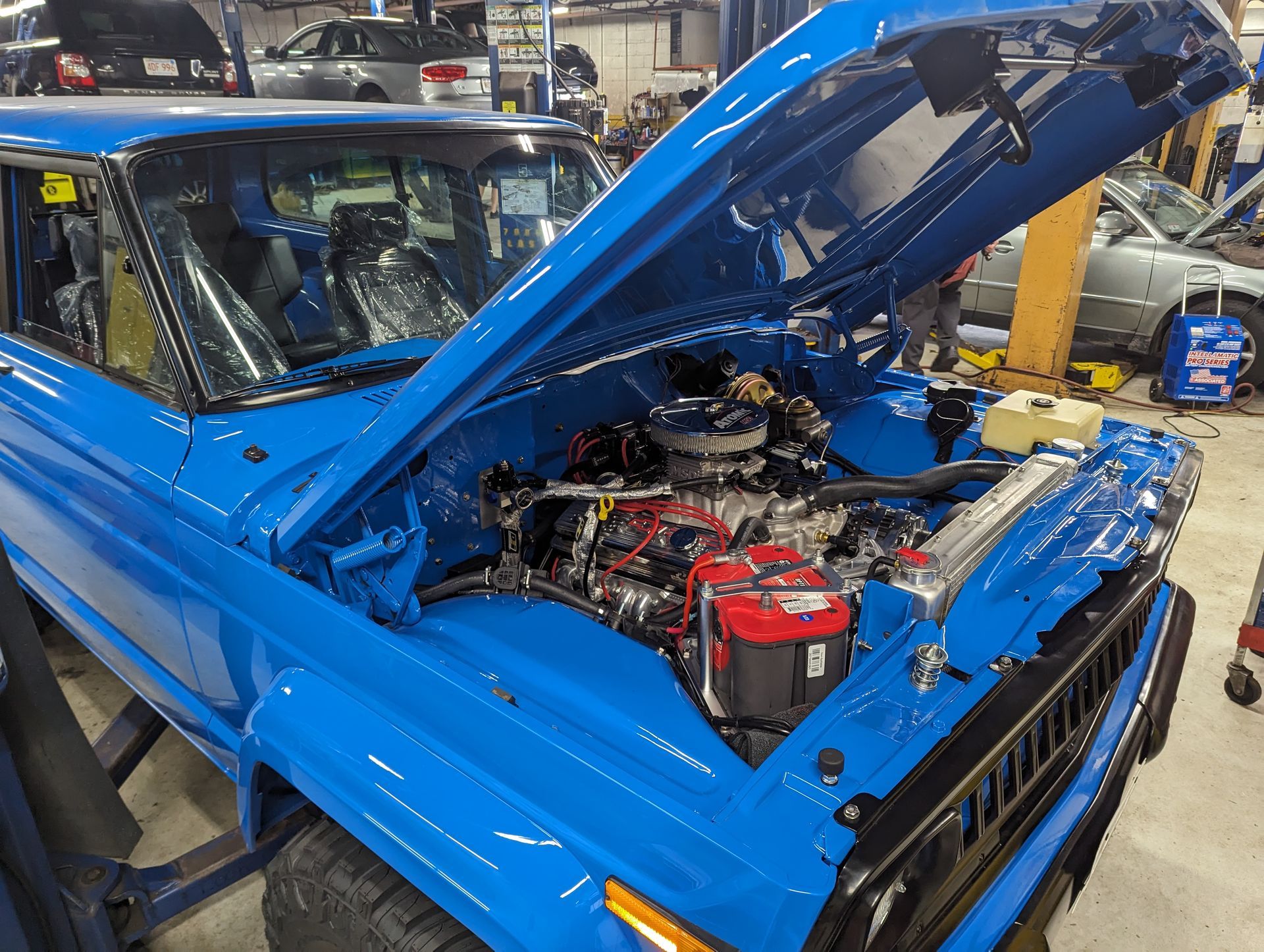 Bright blue vintage Jeep with open hood, engine visible, in a repair shop. | Autobahn Performance