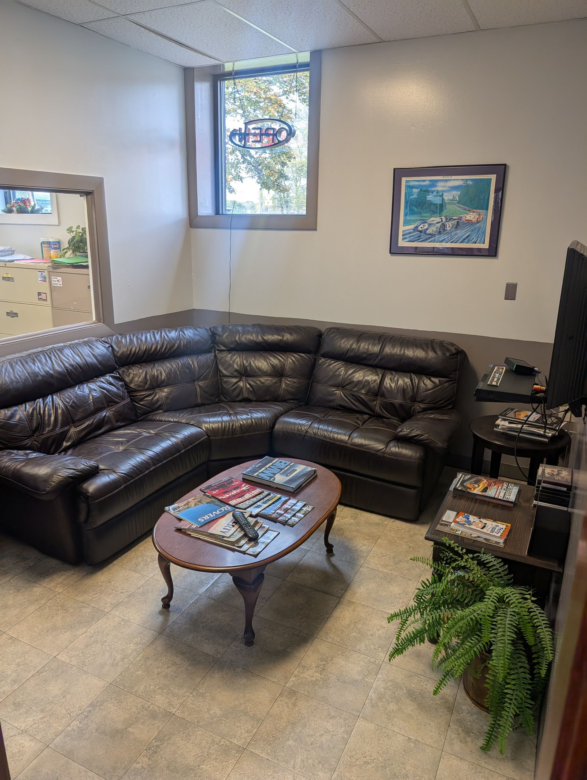 Waiting area with leather sectional sofa, coffee table with magazines, small TV, and a potted plant. | Autobahn Performance Inc