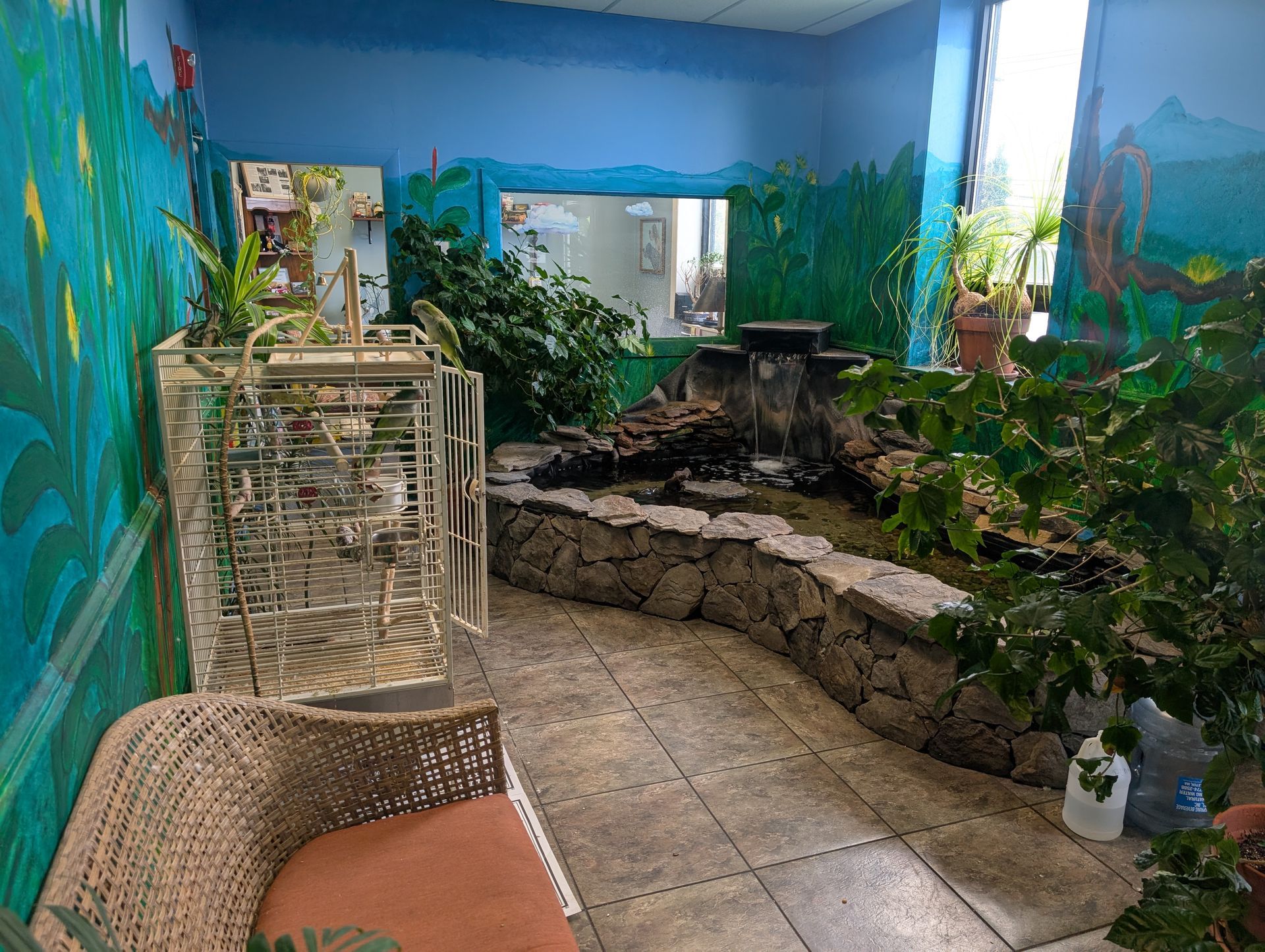 An indoor aviary with a waterfall, plants, and a bird cage, set against painted murals. | Autobahn Performance Inc