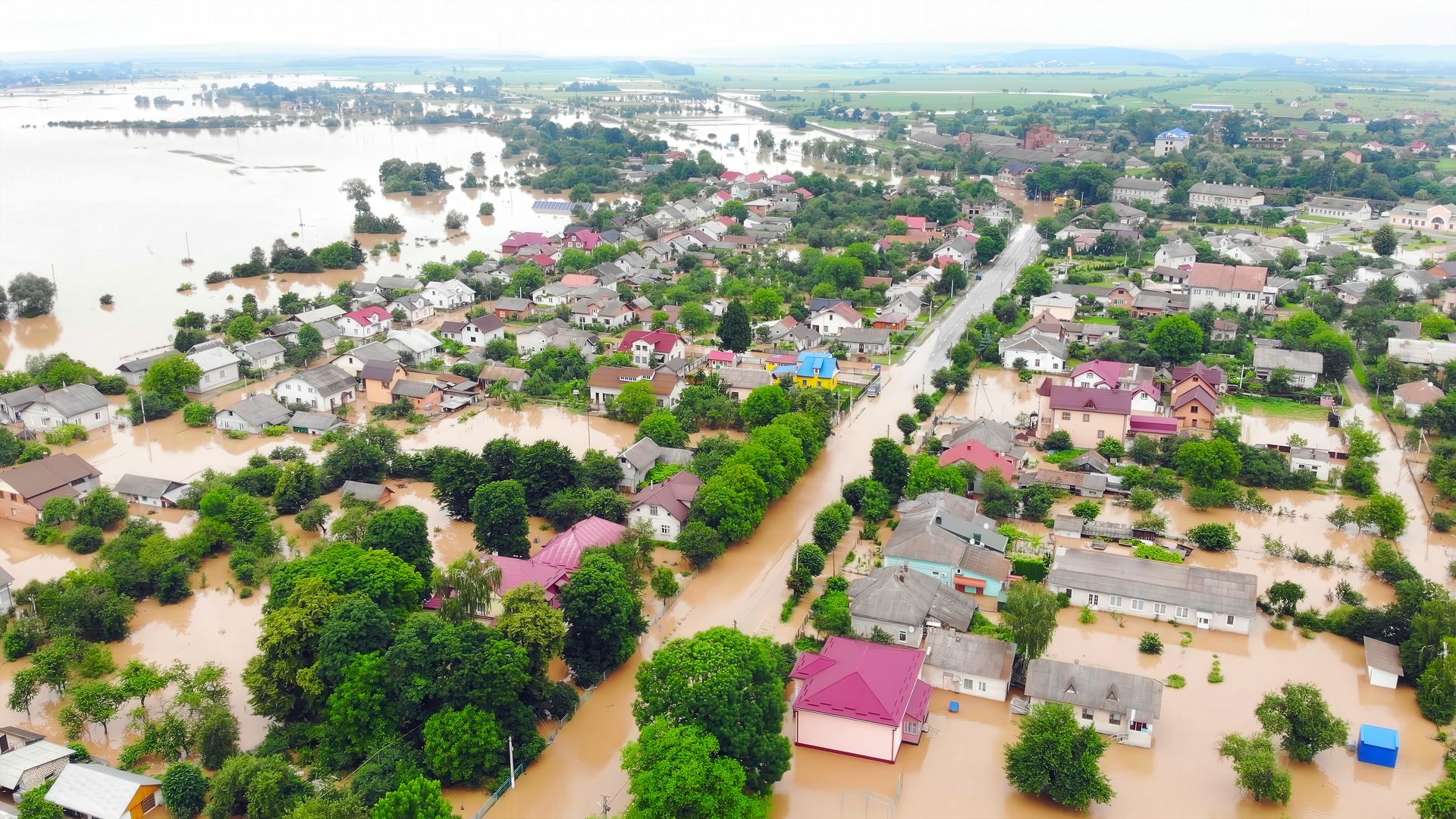 Aerial view of a flooded town with submerged streets, houses, and brown floodwater stretching across the area.