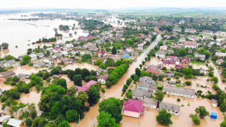 Aerial view of flooded neighborhood with submerged houses, trees, and streets under muddy water