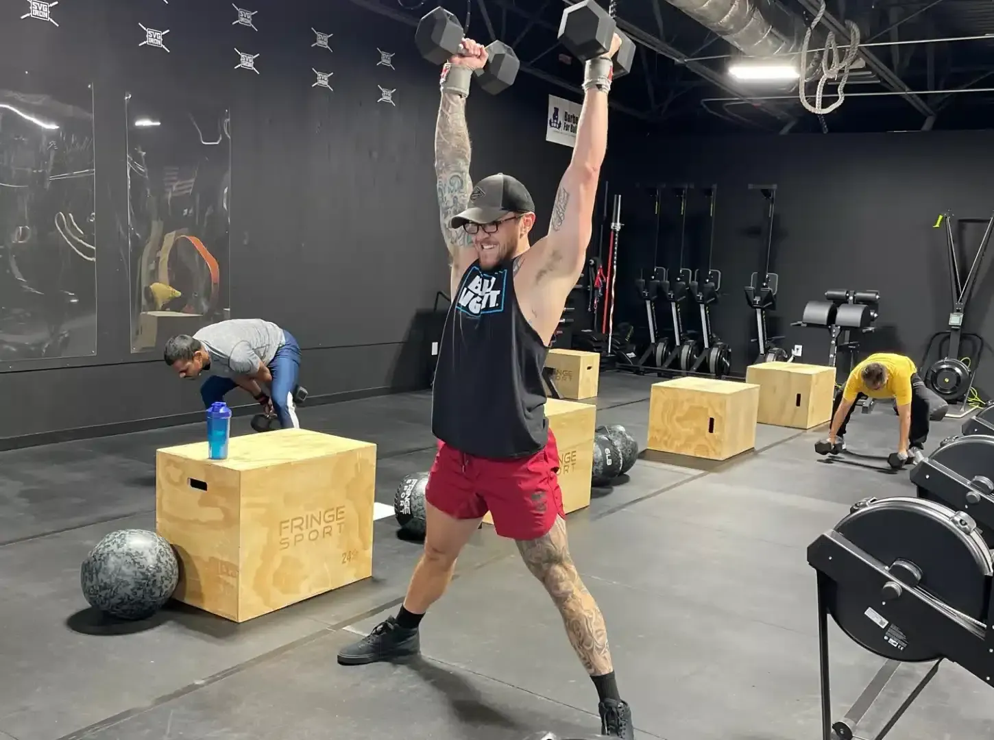 A man is lifting a dumbbell over his head in a gym.