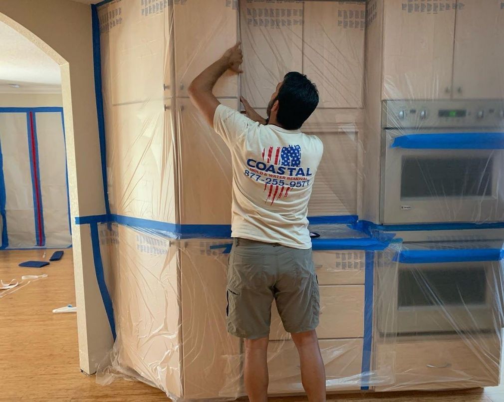Coastal Mold & Water Removal technician in full PPE working on water-damaged walls