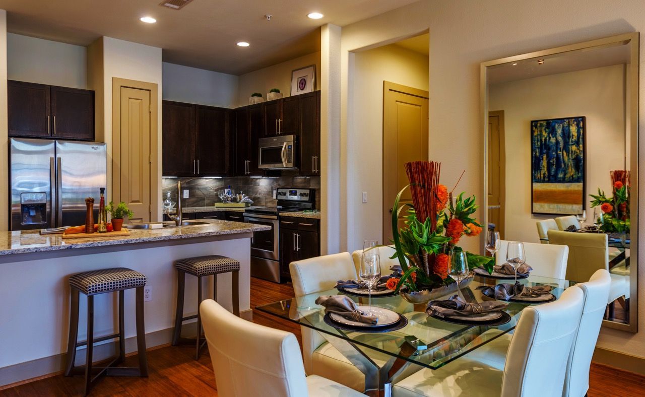 Open kitchen and dining area with dark cabinets, stainless appliances, and glass dining table.