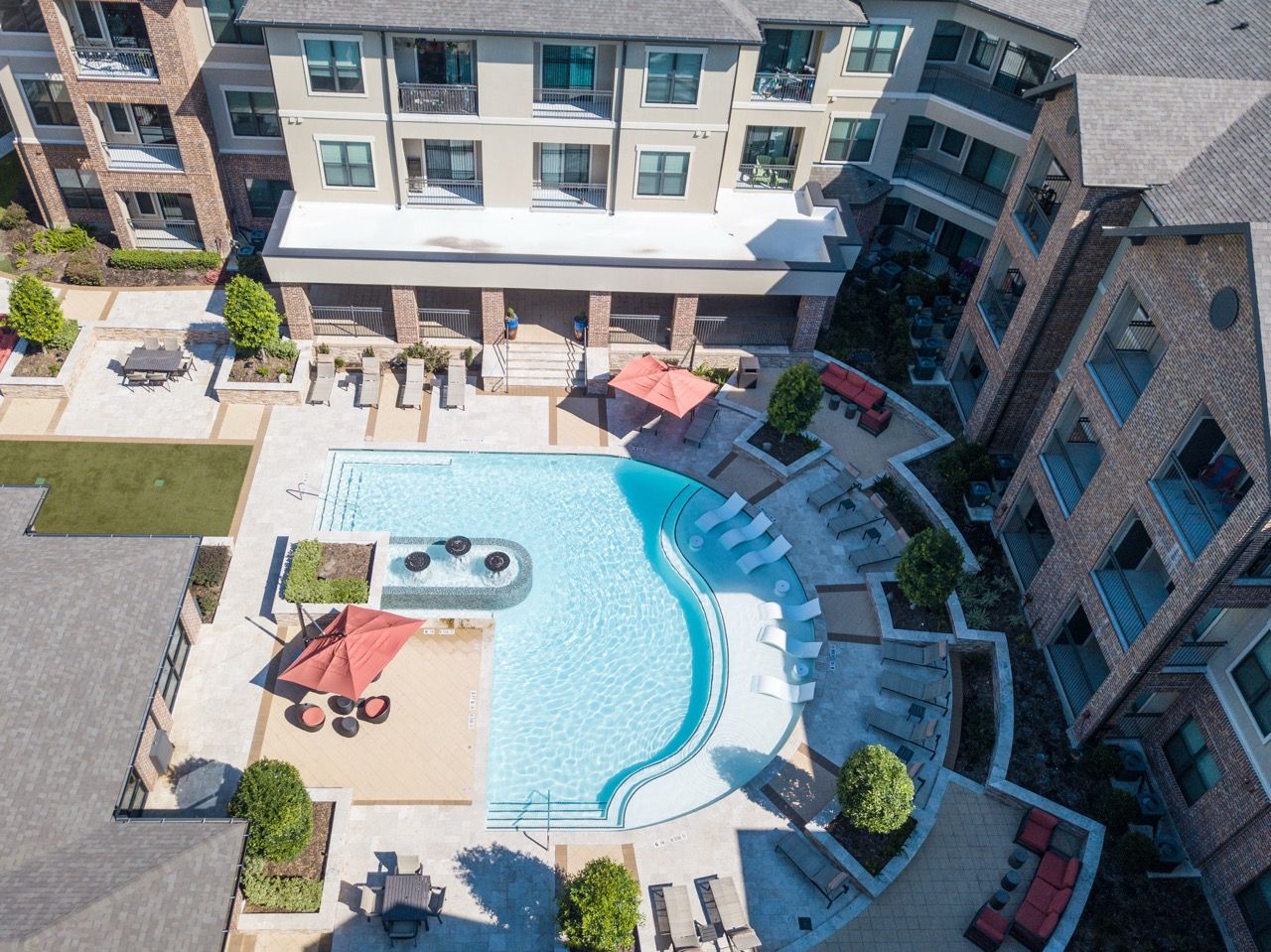 Aerial view of a modern apartment complex pool area with lounge chairs and umbrellas.