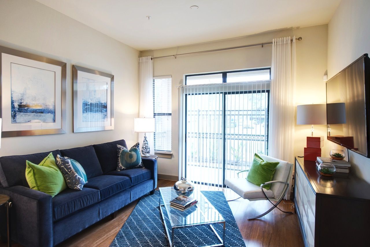 Living room in an apartment with a blue sofa, glass coffee table, and sliding glass doors to a balcony.