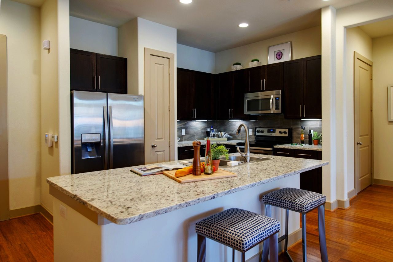Modern kitchen with granite island, stainless steel fridge and microwave, and bar seating.