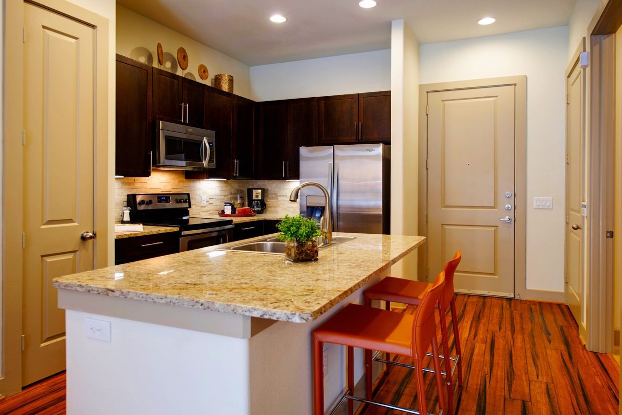Interior apartment kitchen with granite island, dark wood cabinets, and stainless steel appliances.