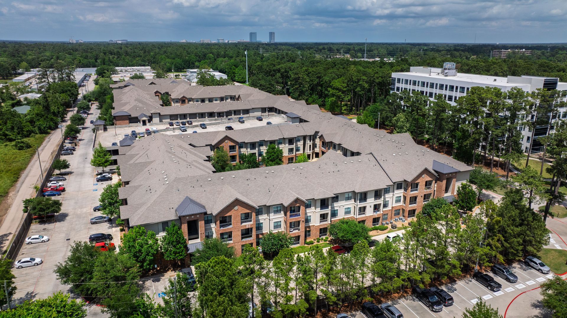 Aerial view of a large apartment complex with parking lots, trees, and a clear blue sky at Olympus Sierra Pines
