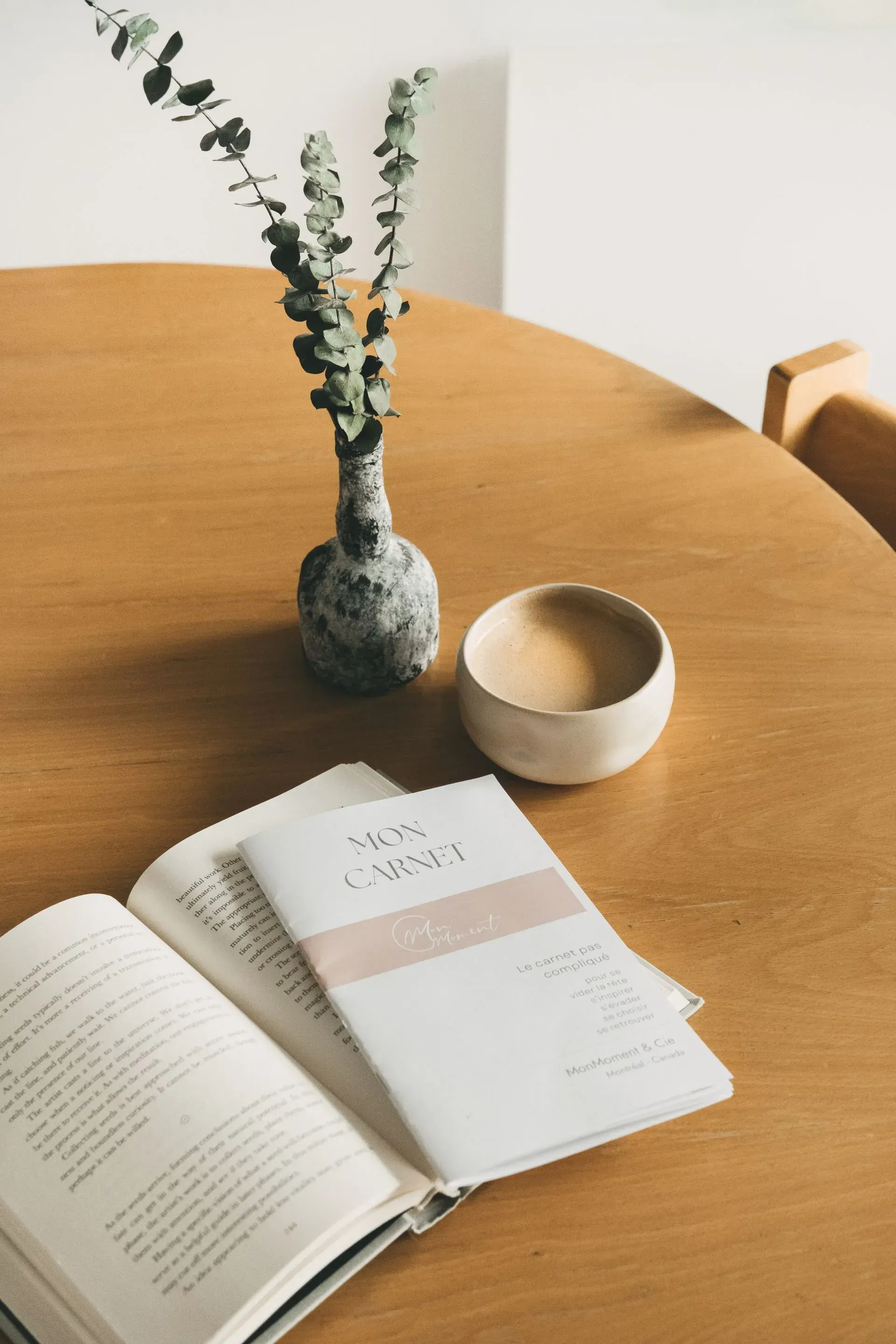 Livre ouvert, carnet, tasse en céramique et vase d'eucalyptus sur une table en bois