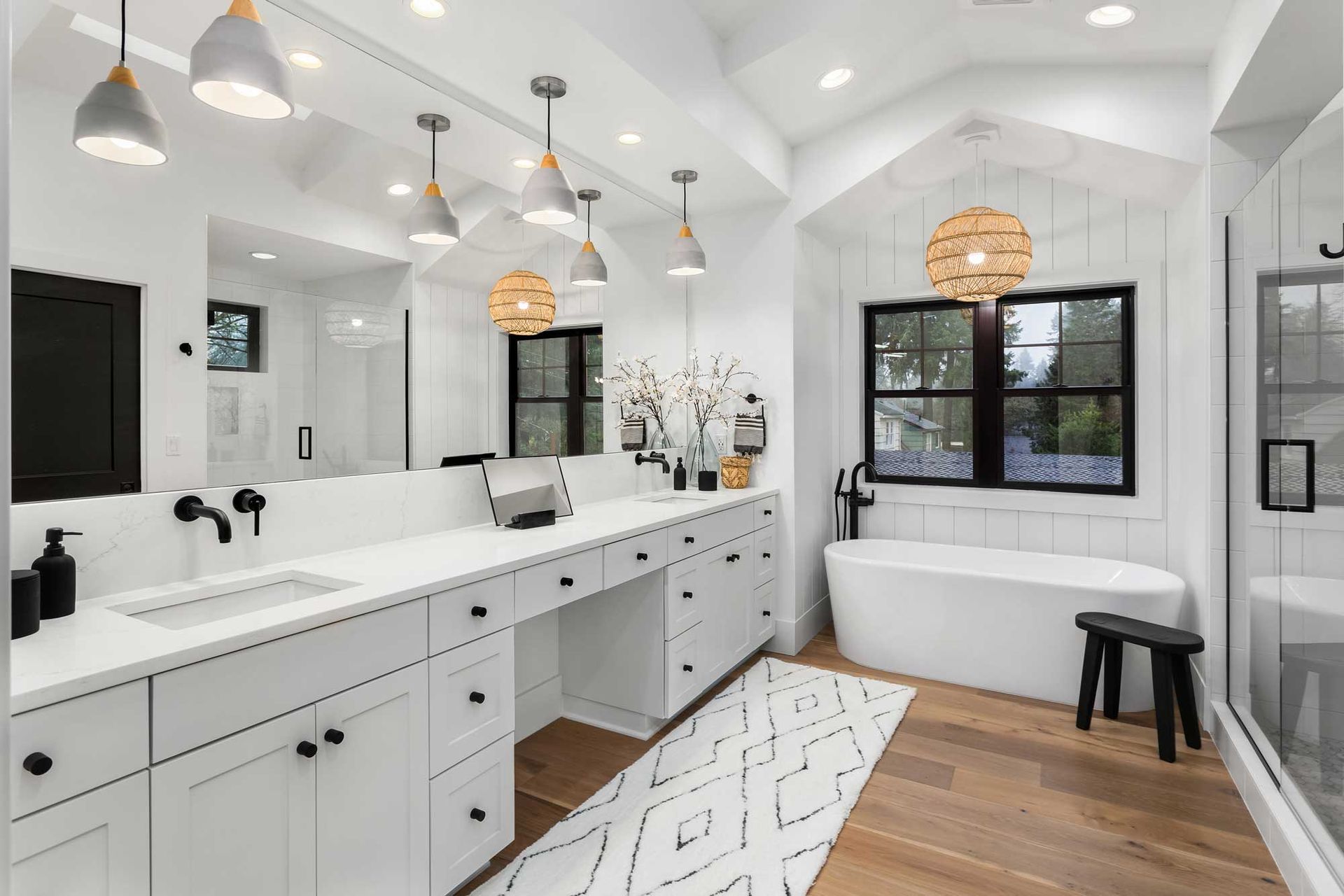 View of a custom bathroom remodel with a double vanity, bathtub, mirror, and hardwood floor. View of a custom bathroom remodel with a double vanity, bathtub, mirror, and hardwood floor.