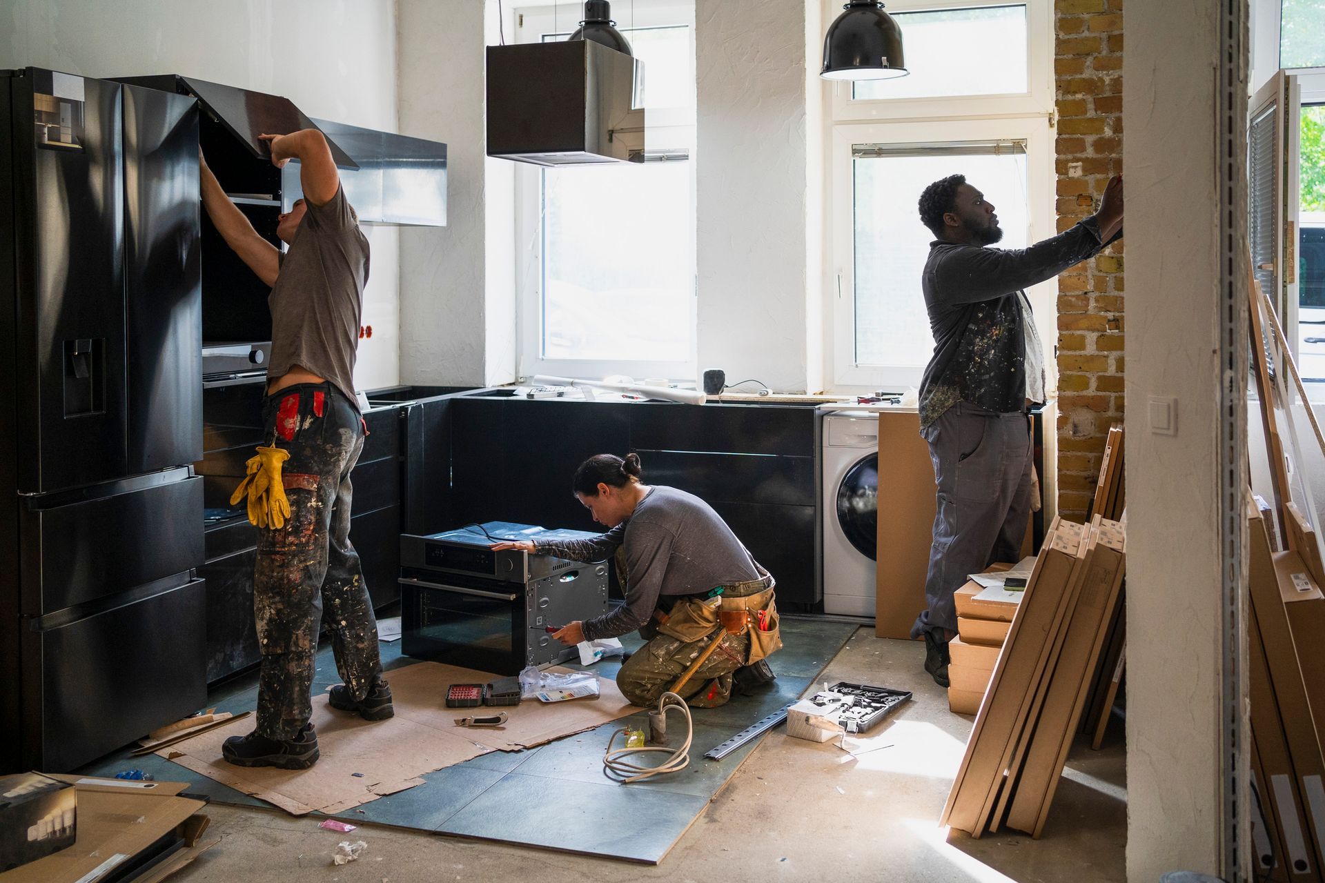 Workers actively renovating a kitchen with tools, cabinets, and appliances in mid-installation.