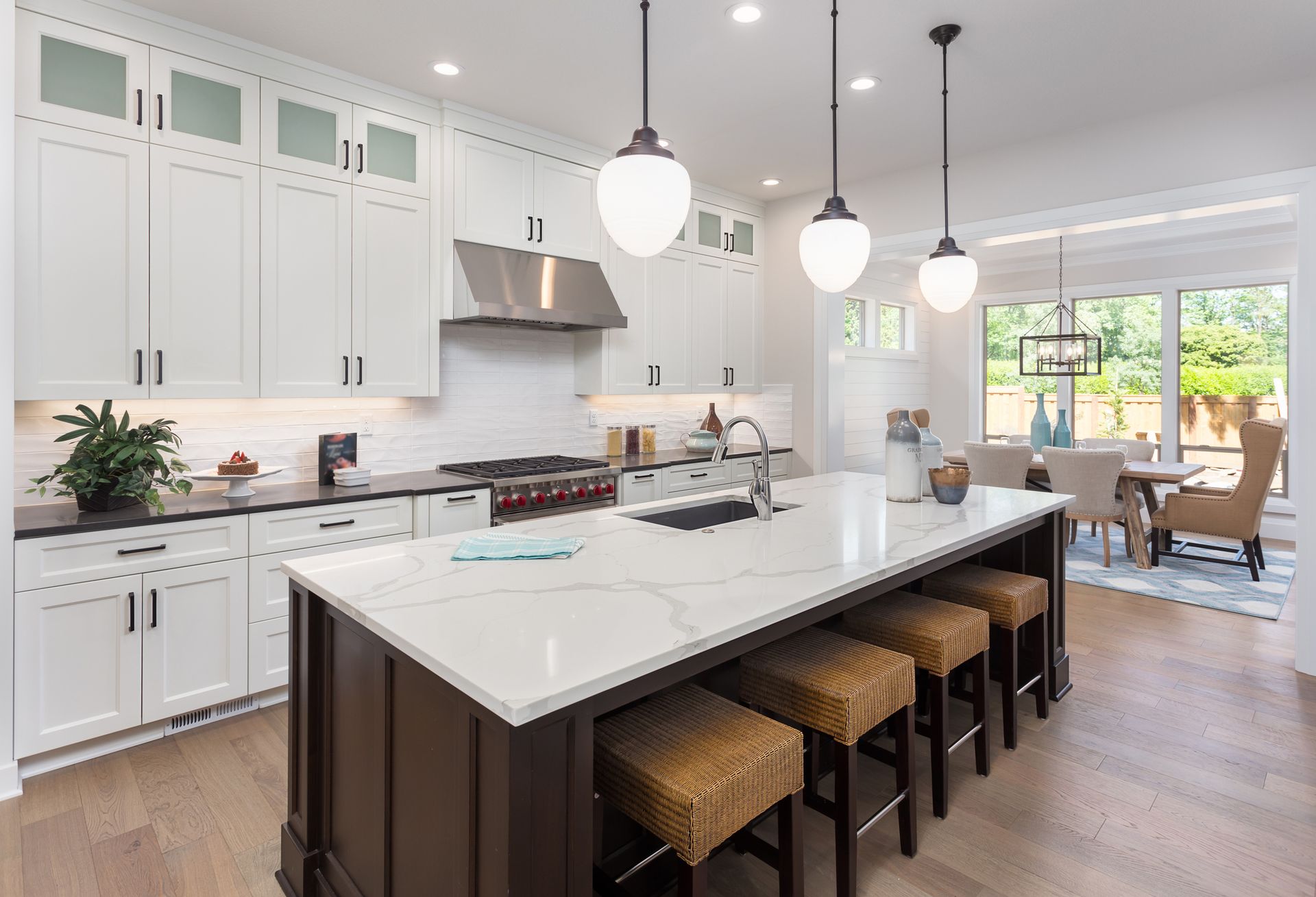 Modern kitchen with white cabinets, marble island, pendant lights, and dining area view.